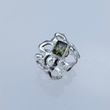 sculptural silver ring with intricate negative spaces and a green gemstone on a light gray background