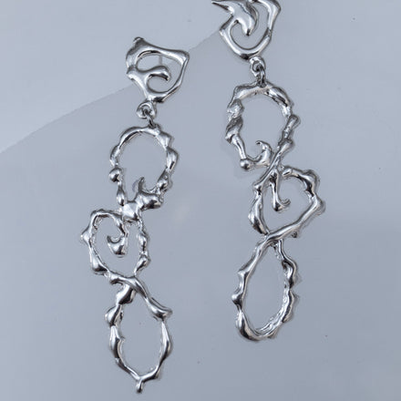 Close-up of handcrafted sterling silver wavy earrings showing irregular texture and movement