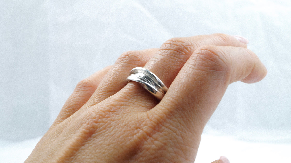 Close-up of Fold 005 worn on a hand, showing its overlapping silver bands