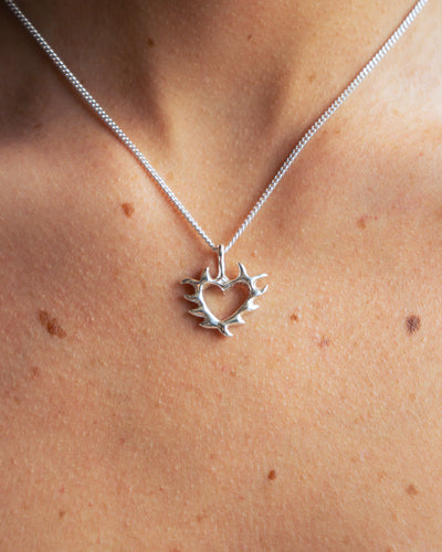 Silver necklace with a heart and leaf pendant on a person's neck.