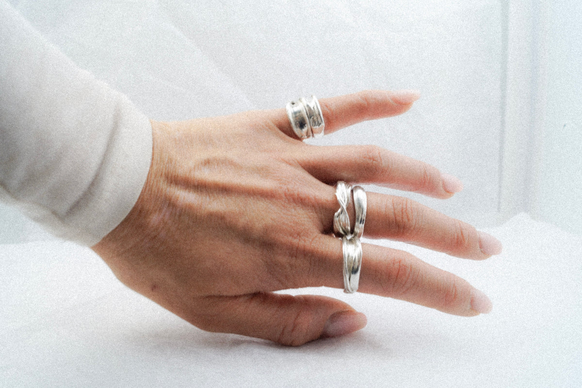 Hand wearing Fold 003 with a stack of sculptural sterling silver rings