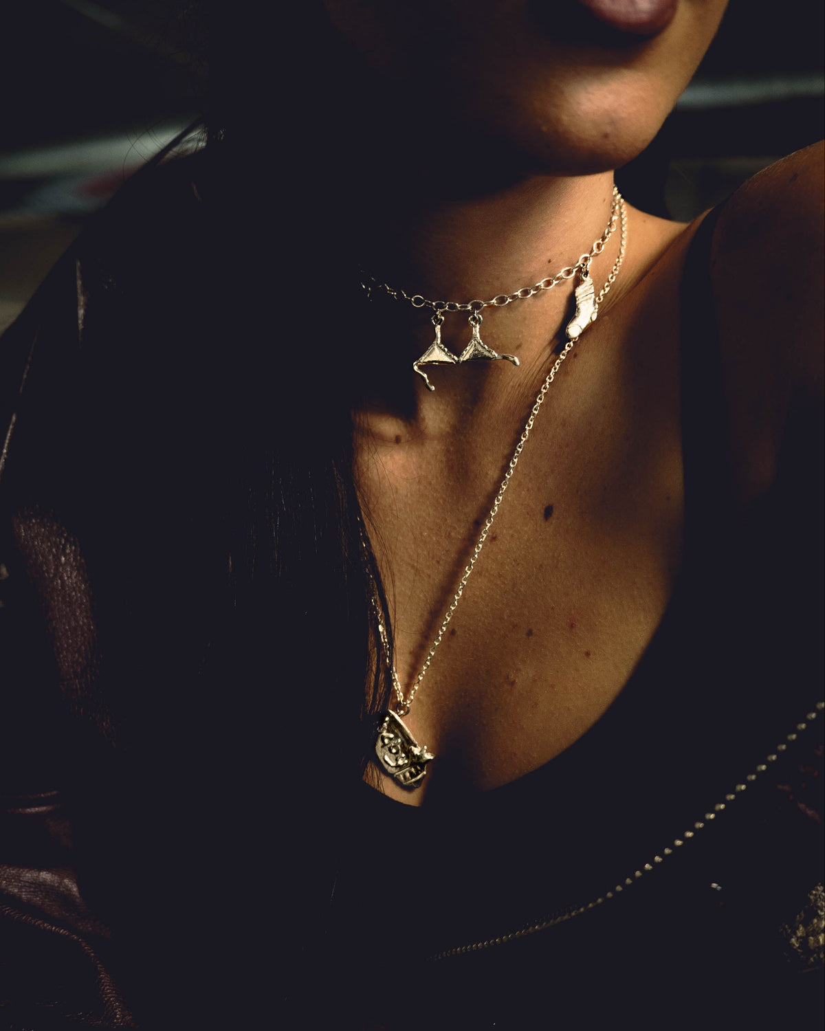 Close-up of a person wearing sterling silver necklaces, featuring sterling silver bra and sock charms