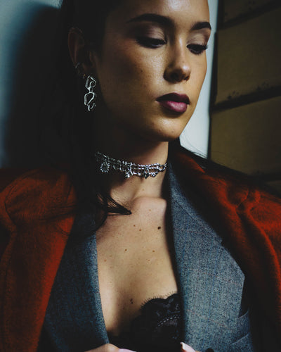 Woman wearing a red coat and gray sweater with a dark top underneath, statement shiny sterling silver sculptural stud earrings