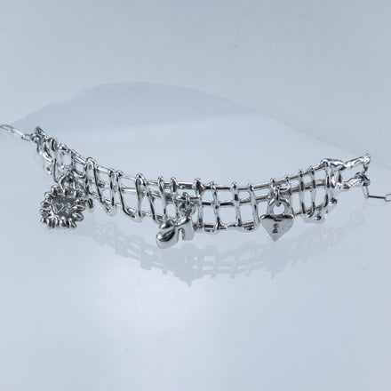 Sterling silver charm necklace with sculptural shoe, stamp, and heart lock charms on chain. light grey background