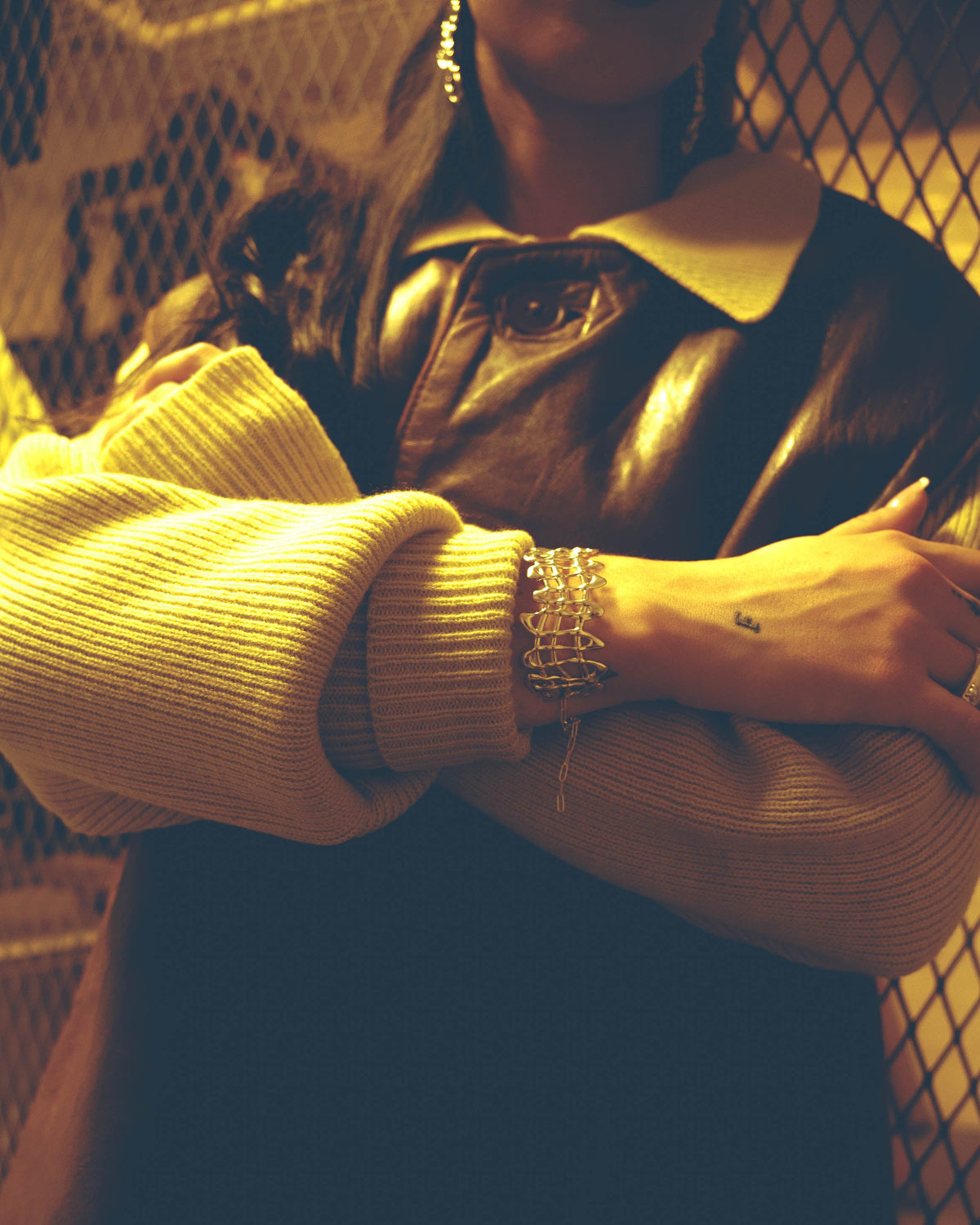 Person wearing a yellow sweater and leather jacket with a blurred background and statement sterling silver bracelet
