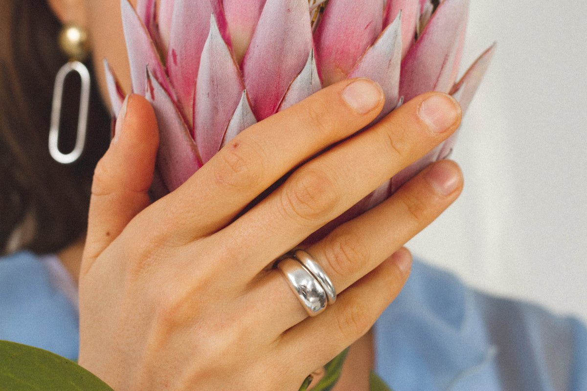 Thin and Thick sterling silver Blob Rings stacked on a hand holding a flower